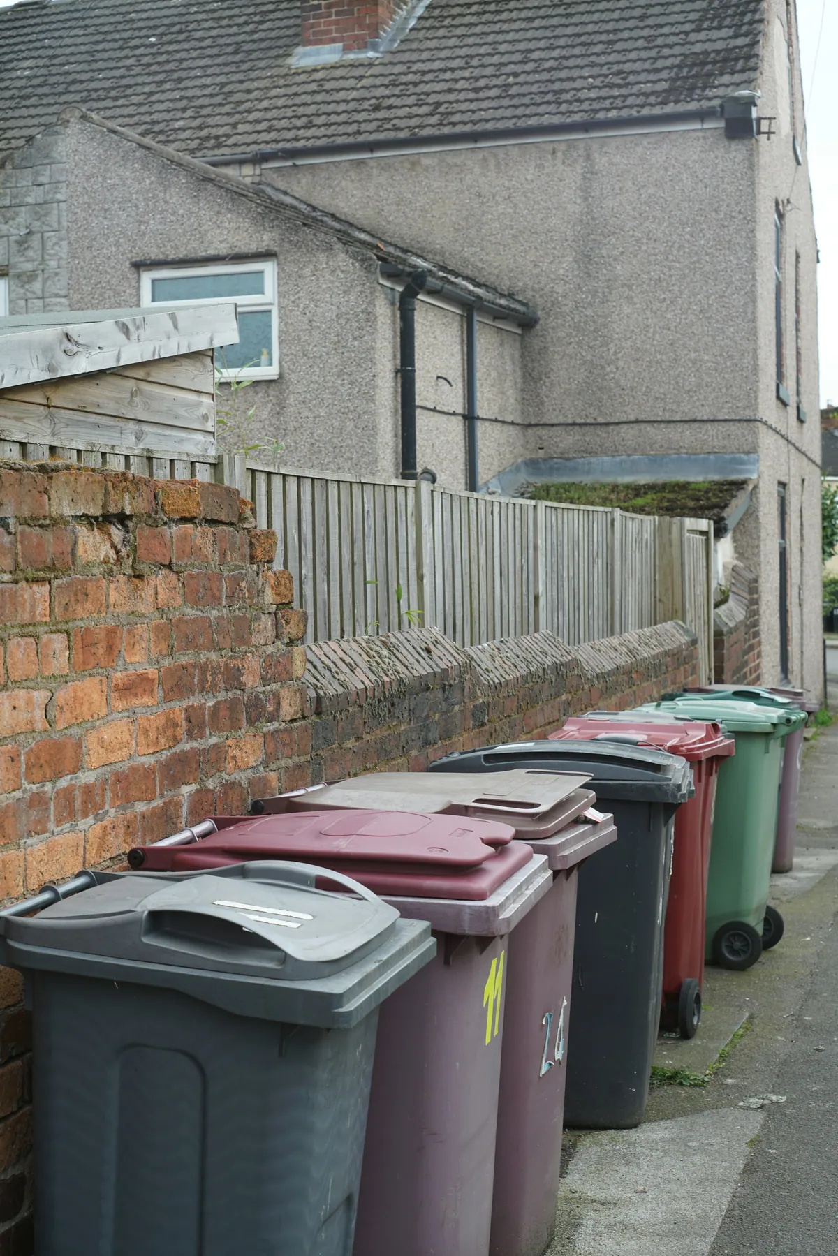 Colourful wheelie bins lined up along a brick wall