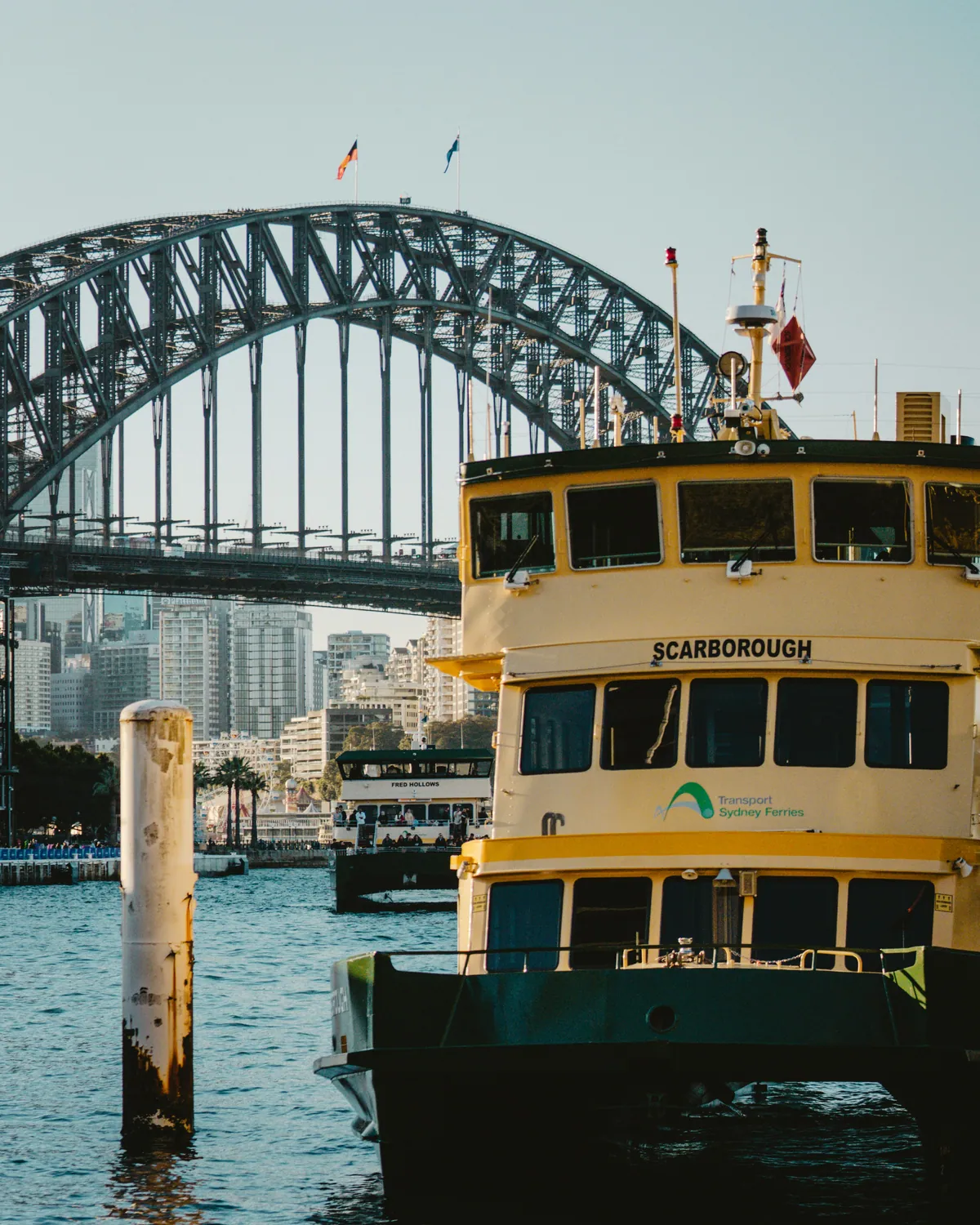 A green and yellow Sydney ferry at the wharf under the Harbour Bridge