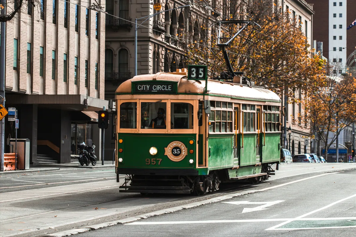 A green and gold Melbourne heritage tram turning through a city street
